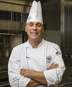 Chef Doug Overes smiles, wearing his chef hat and whites