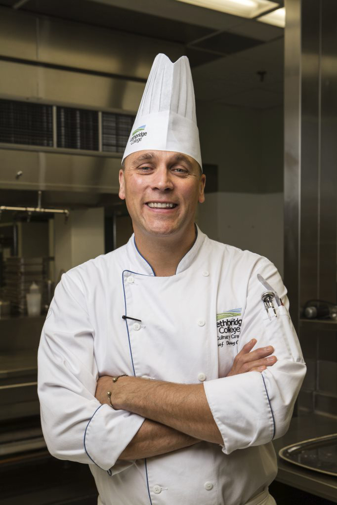 A man smiles at the camera. He is wearing chef whites and hat.