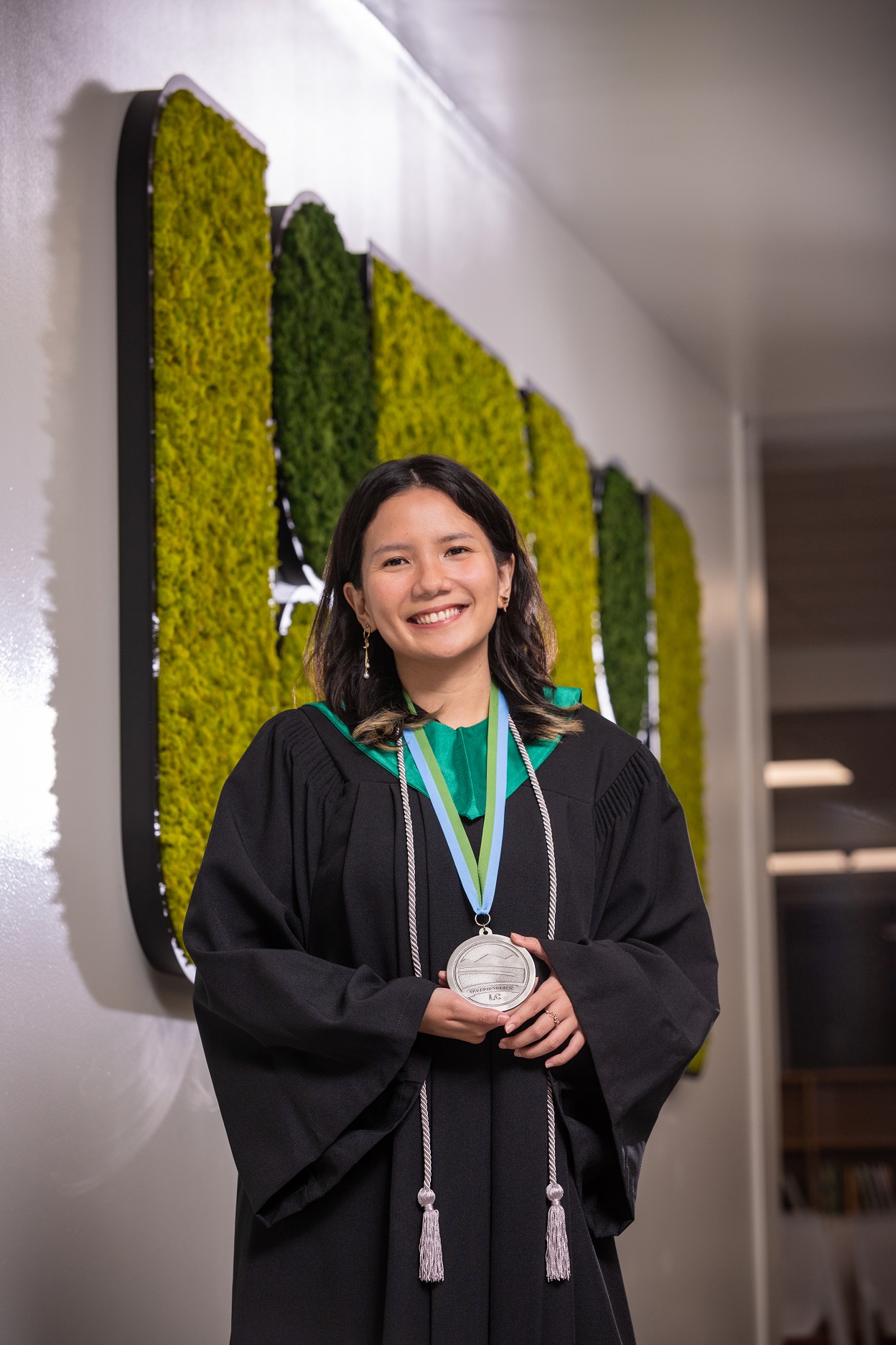 A young woman wearing a graduation gown smiles for the camera