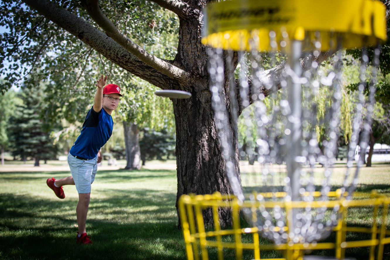 a person tosses a disc golf frisbee into the basket