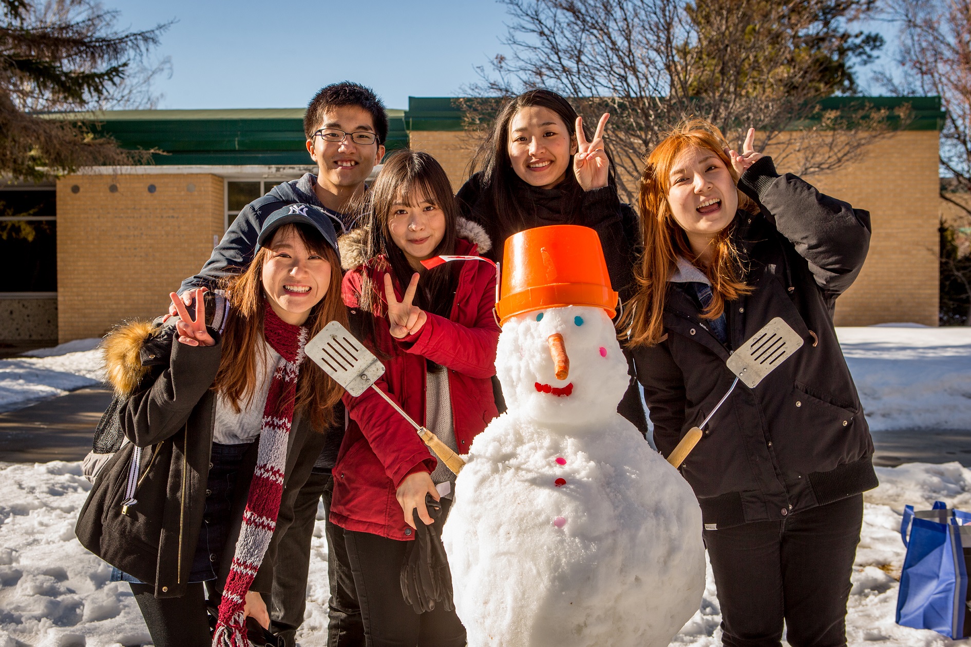 a group of students smile, standing behind a snowman