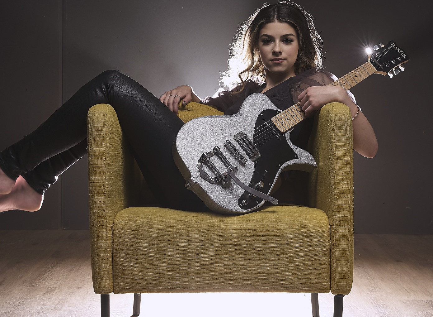 A woman lays across a chair holding a guitar