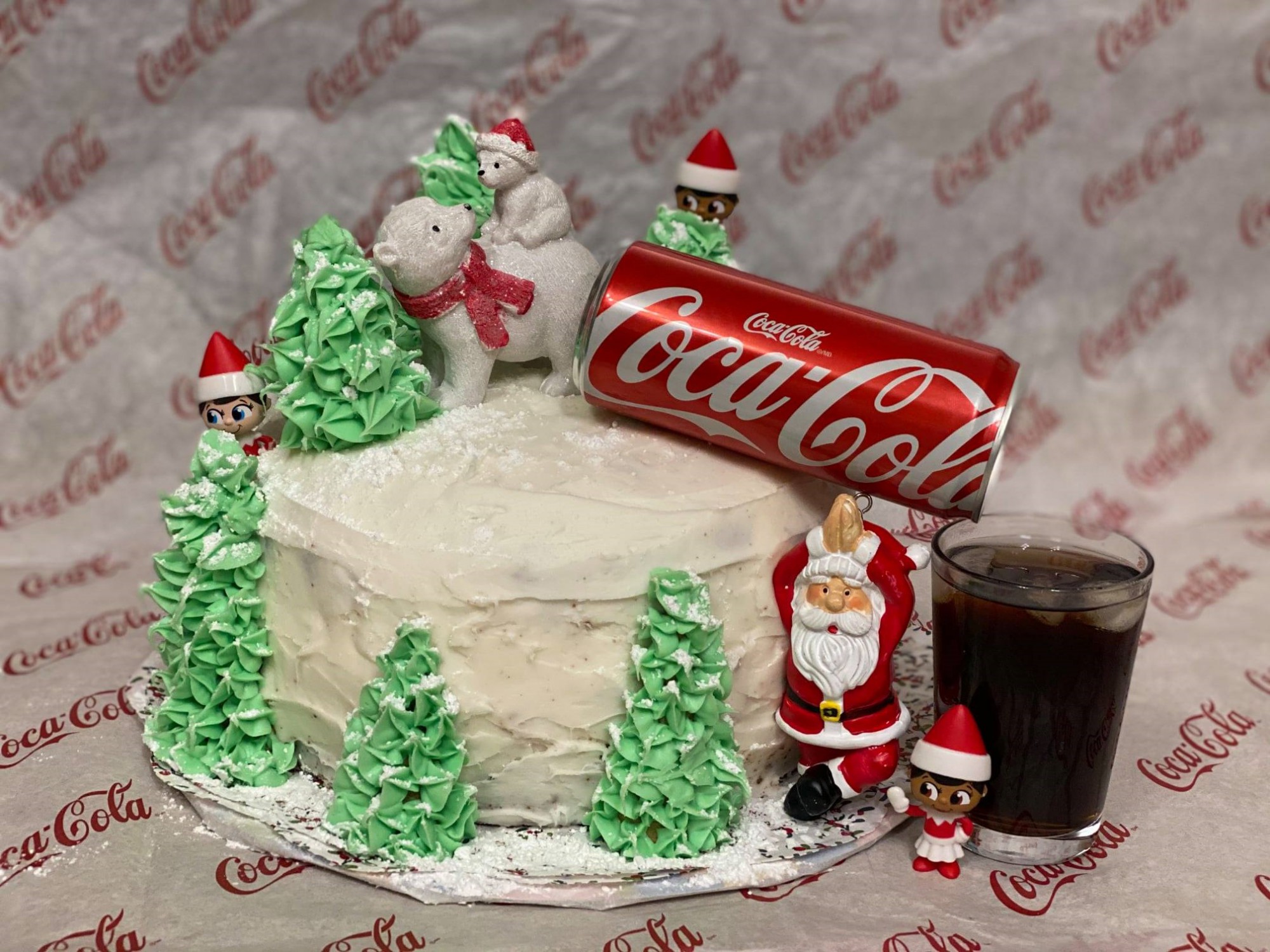 a cake decorated with a Santa, trees and a can of Coca-Cola