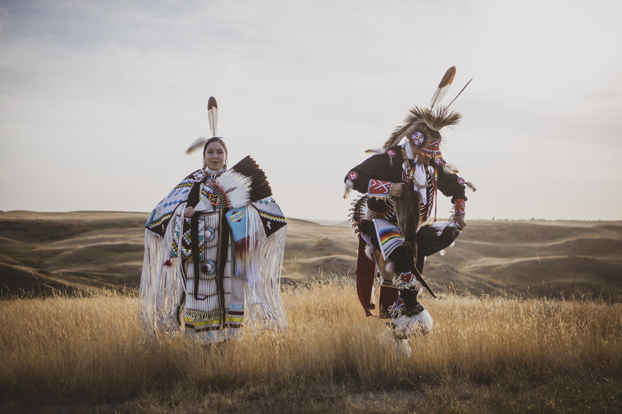 two Indigenous dancers, a man and a woman, dance on the coulees