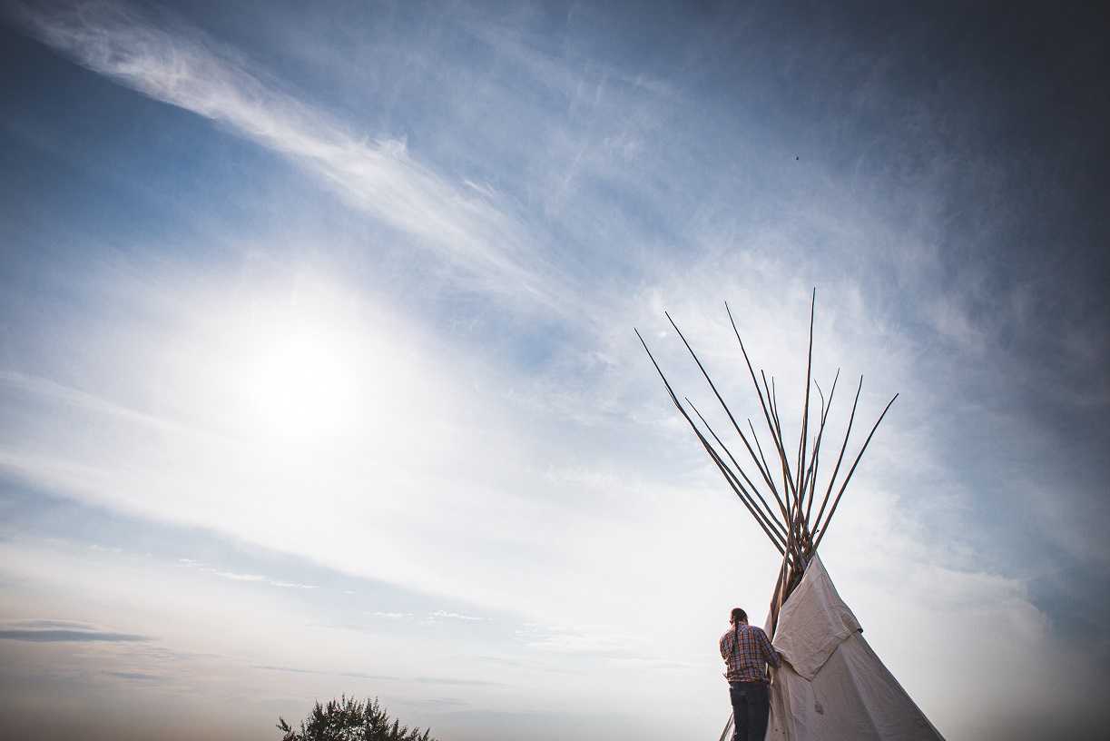 a man stands in front of a tipi