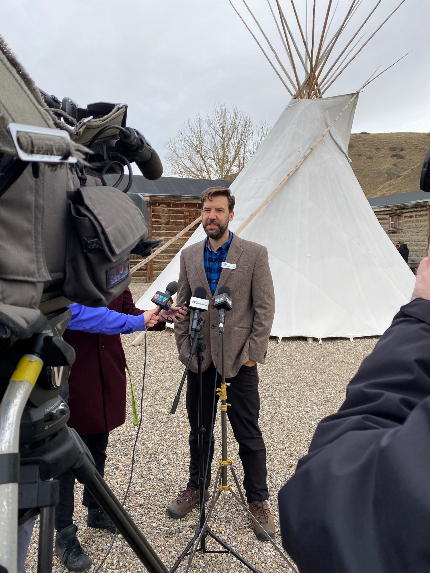 a man in a suit jacket standing in front of a teepee, speaks to reporters
