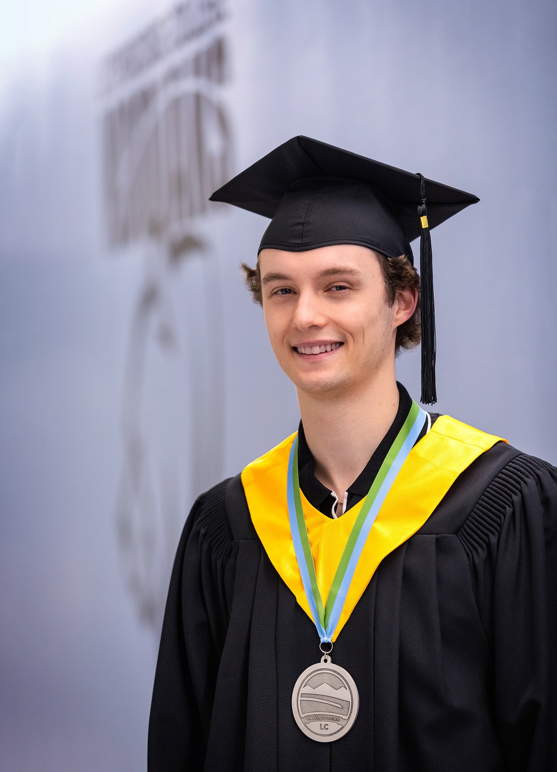 A young man wearing a graduation cap and gown smiles for the camera.
