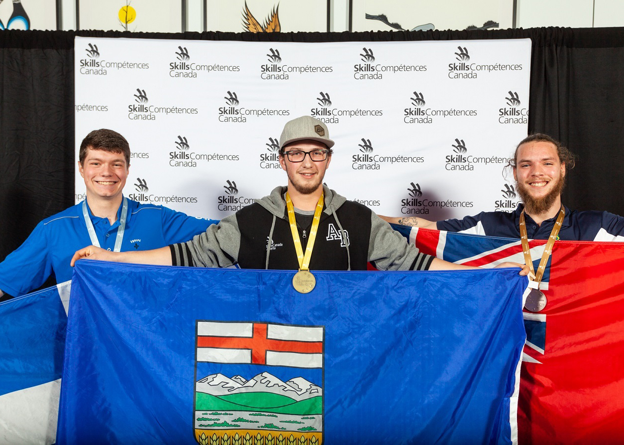 A man wearing a gold medal around his neck holds an Alberta flag and smiles.