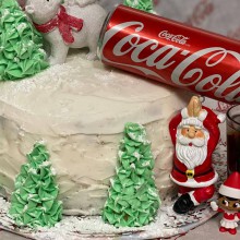 a cake decorated with a Santa, trees and a can of Coca-Cola