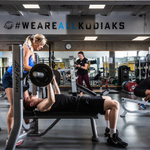one person spots another person as they lift weights in a fitness centre
