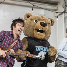 A mascot bear on stage with a man playing a guitar