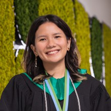 A young woman wearing a graduation gown smiles for the camera