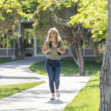 A woman wearing a backpack walks outside on campus