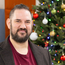 College instructor Karl Rejman stands in front of a Christmas tree.