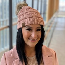 a woman in a pink jacket and toque, smiles for the camera
