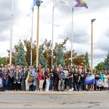a large group of people gathers in front of a raised flag.