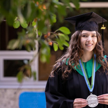 A woman in a graduation cap and gown smiles for camera.