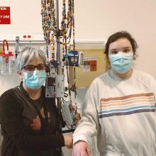 A teenaged girl and her mother wear surgical masks in a hospital room.