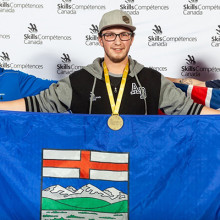 A man with a gold medal around his neck holds an Alberta flag.