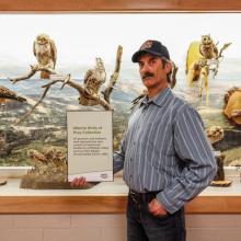 Peter Balagus stands in front of a display of birds he donated and holds a plaque about the donation.