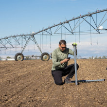 Lethbridge College researcher using smart phone next to irrigation equipment at the Lethbridge College Research Farm.